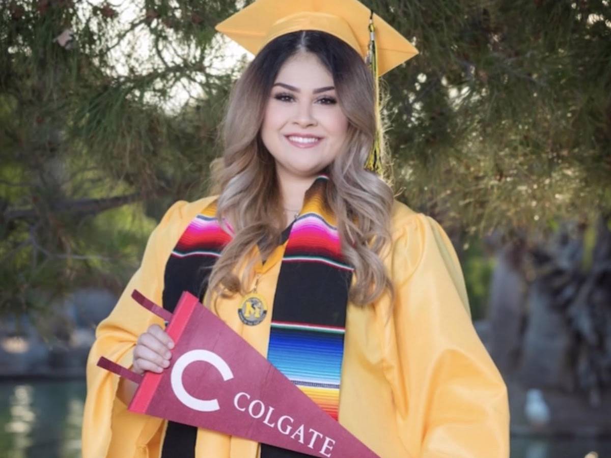 Lizeth in her cap and gown at her high school graduation holding a Colgate pennant.